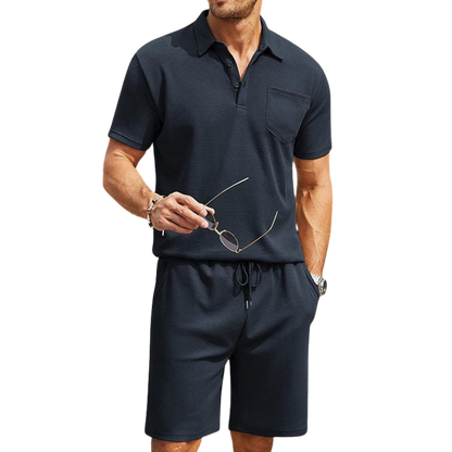 Uomo in completo estivo casual nero, con polo e pantaloncini, tiene occhiali da sole. Moda maschile, abbigliamento estivo elegante e confortevole.