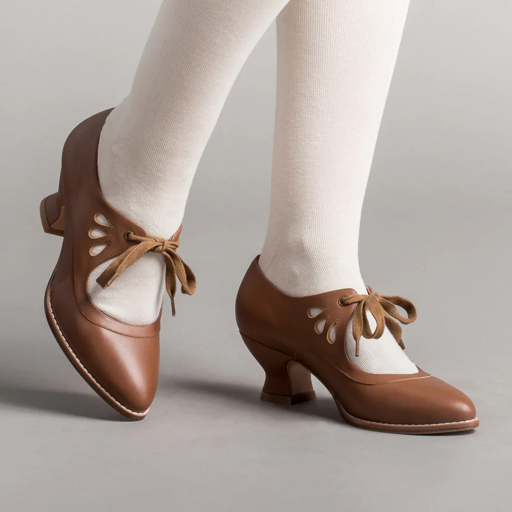 Scarpe da ballo vintage marroni con lacci, tacco medio e dettagli traforati, indossate con calze bianche. Eleganza retrò per danza classica.