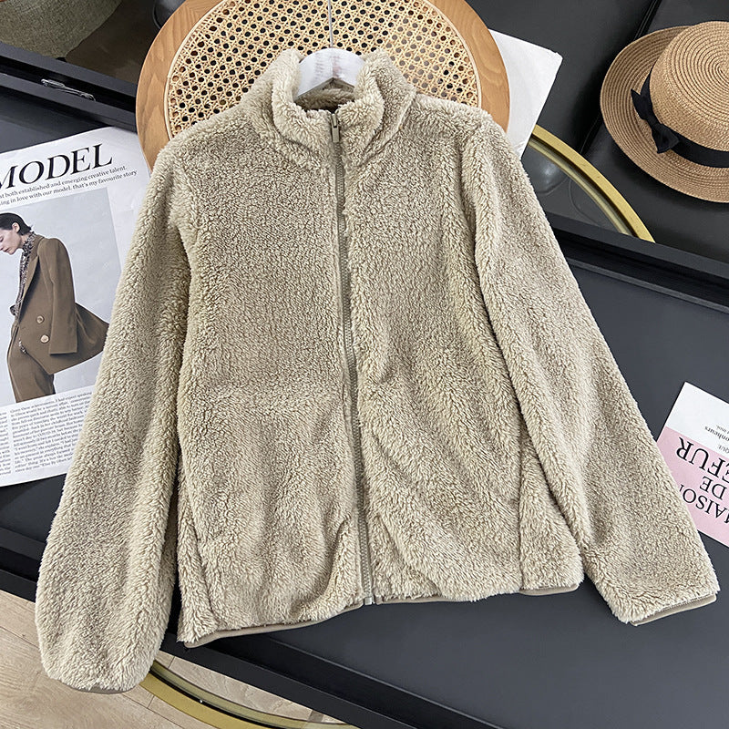 Giacca in pile beige su tavolo nero, accanto a cappello di paglia e rivista di moda. Abbigliamento invernale caldo e morbido, stile casual.