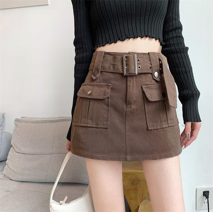 Donna con gonna marrone a vita alta con tasche e cintura, maglione nero a coste, borsa bianca. Moda autunnale casual, stile urbano.