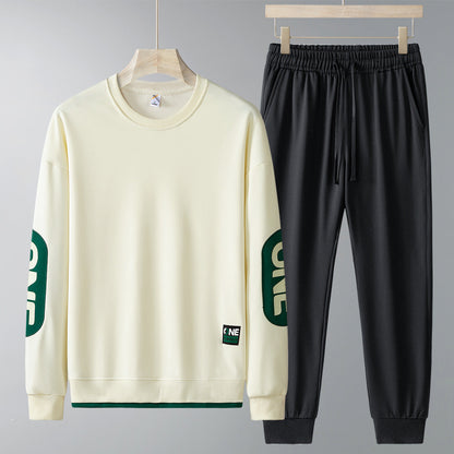 Set abbigliamento sportivo uomo: felpa beige con scritta verde sulle maniche e pantaloni neri. Moda casual, comodo per palestra e tempo libero.