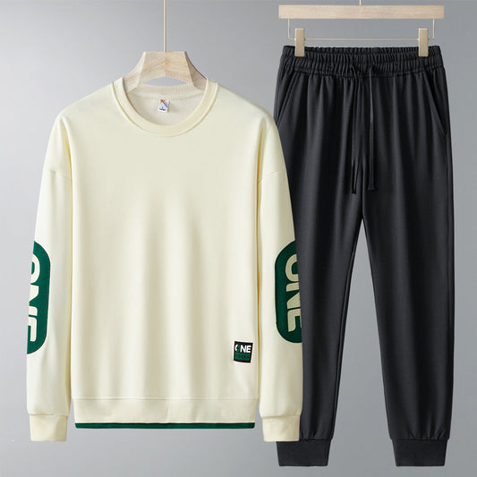 Set abbigliamento sportivo uomo: felpa beige con scritta verde sulle maniche e pantaloni neri. Moda casual, comodo per palestra e tempo libero.