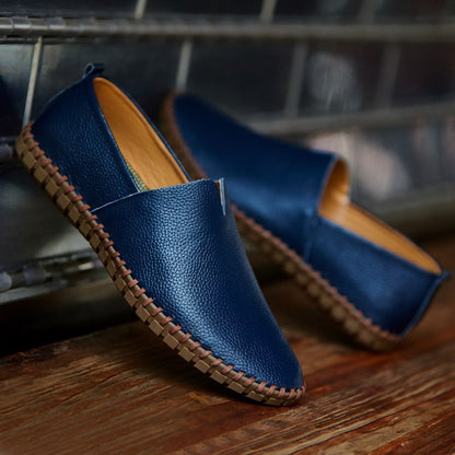 Scarpe mocassini in pelle blu, suola in gomma marrone, posizionate su una superficie di legno. Calzature eleganti e casual per uomo.