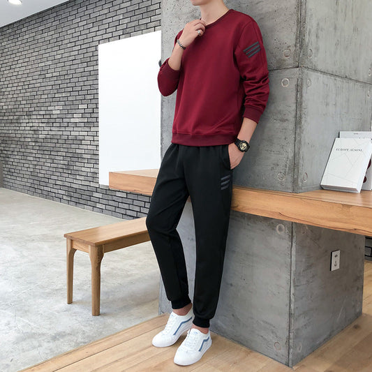Uomo in tuta sportiva rossa e nera, scarpe bianche, posa moderna in interno minimalista. Abbigliamento casual, moda maschile, stile urbano.