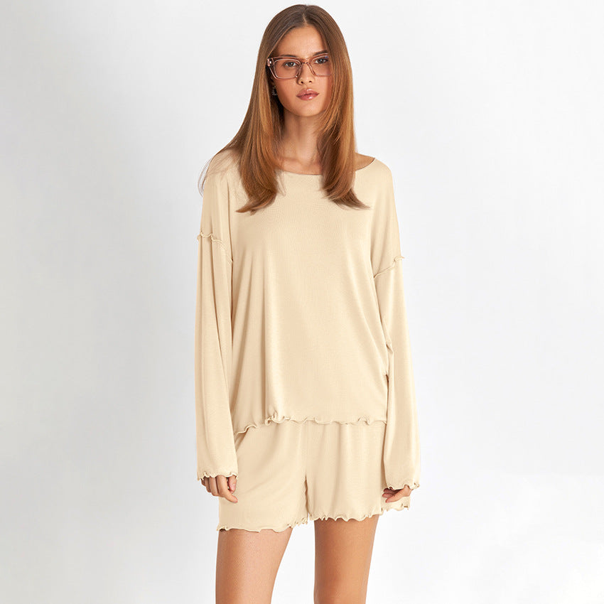 Donna con pigiama beige a maniche lunghe, occhiali da vista, sfondo bianco. Moda comoda, abbigliamento da casa elegante, stile minimalista.