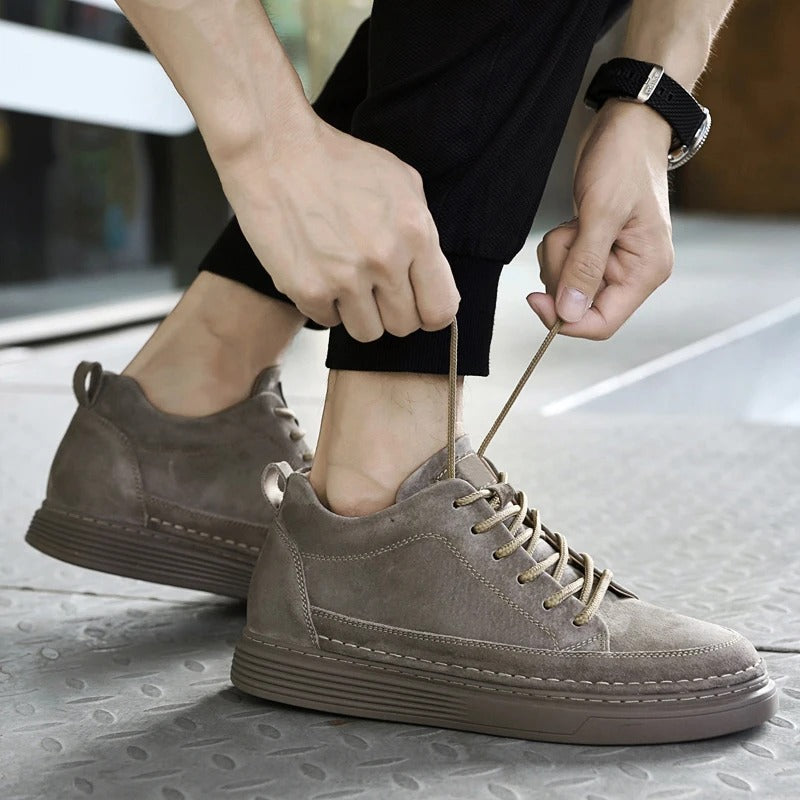 Scarpe da ginnastica uomo in pelle scamosciata grigia, lacci allacciati, suola spessa, stile casual, moda urbana, pavimento metallico.