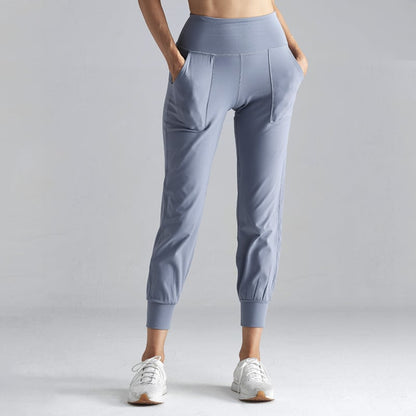 Pantaloni sportivi donna grigi, vita alta, tasche laterali, abbinati a scarpe da ginnastica bianche. Abbigliamento fitness comodo ed elegante.