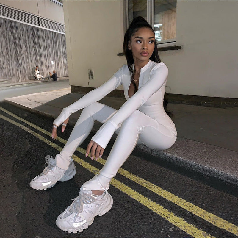 Giovane donna in tuta bianca e sneakers seduta su strada urbana di notte, moda streetwear, look casual, capelli lunghi raccolti, atmosfera metropolitana.