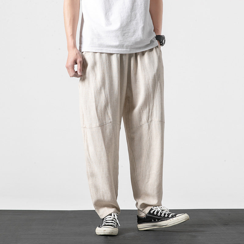Pantaloni larghi in lino beige, indossati con t-shirt bianca e sneakers nere. Moda casual uomo, stile estivo, abbigliamento comodo.