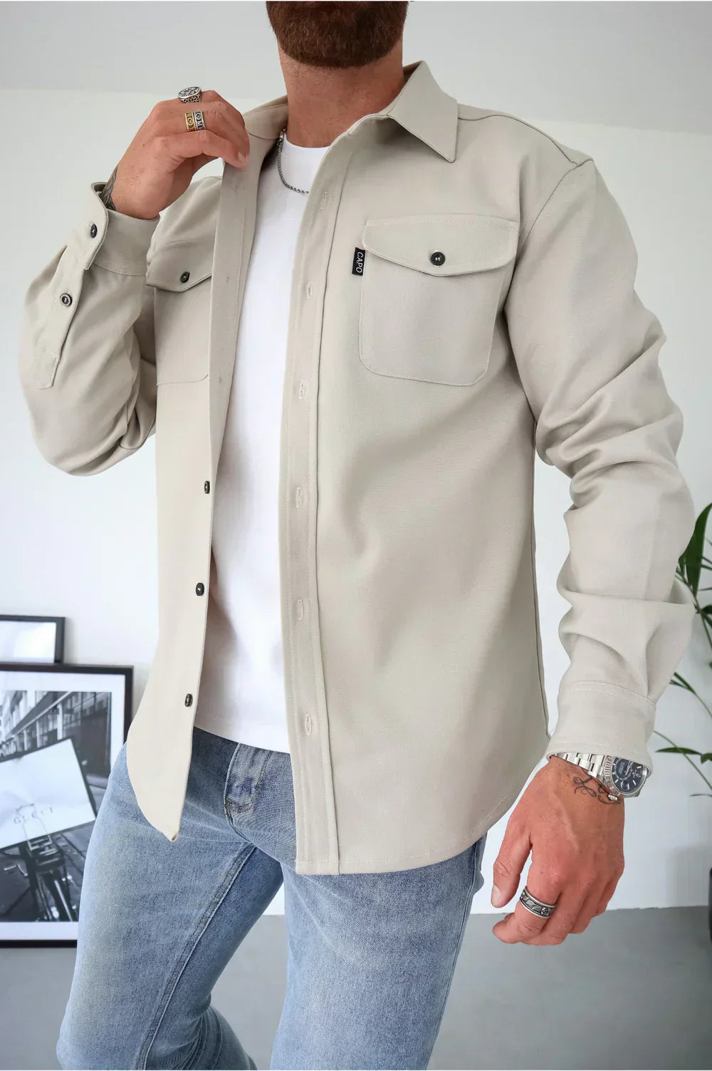 Camicia beige da uomo con tasche frontali, indossata sopra una maglietta bianca e jeans. Moda casual maschile, stile moderno ed elegante.
