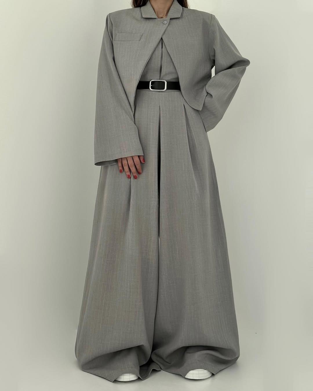 Donna in elegante completo grigio oversize, giacca e pantaloni larghi, cintura nera, scarpe bianche. Moda contemporanea, abbigliamento femminile chic.