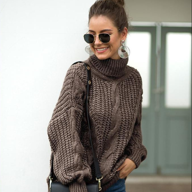 Donna sorridente con occhiali da sole, indossa un maglione a collo alto marrone e orecchini grandi. Moda autunnale, stile casual chic.