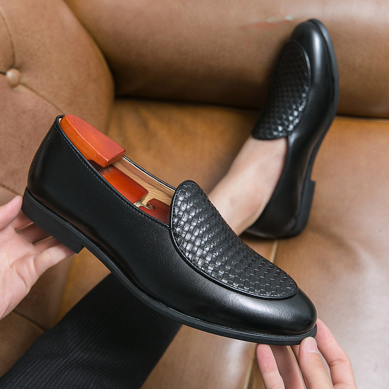 Scarpe eleganti da uomo in pelle nera con motivo intrecciato, su divano marrone. Calzature formali di lusso, stile classico e raffinato.