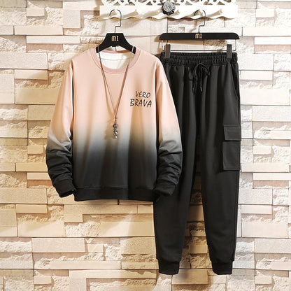 Completo tuta uomo sfumato nero e beige, scritta "Vero Brava", pantaloni cargo, felpa casual, moda streetwear, appeso su sfondo muro mattoni.