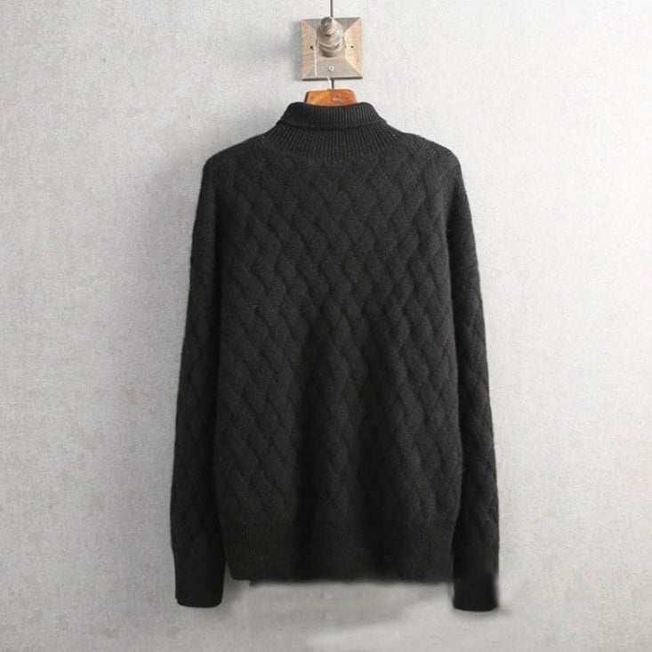 Maglione nero in lana a trecce appeso a un gancio su sfondo grigio. Design elegante e caldo, ideale per l'inverno. Moda uomo, abbigliamento casual.