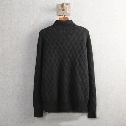 Maglione nero in lana a trecce appeso a un gancio su sfondo grigio. Design elegante e caldo, ideale per l'inverno. Moda uomo, abbigliamento casual.