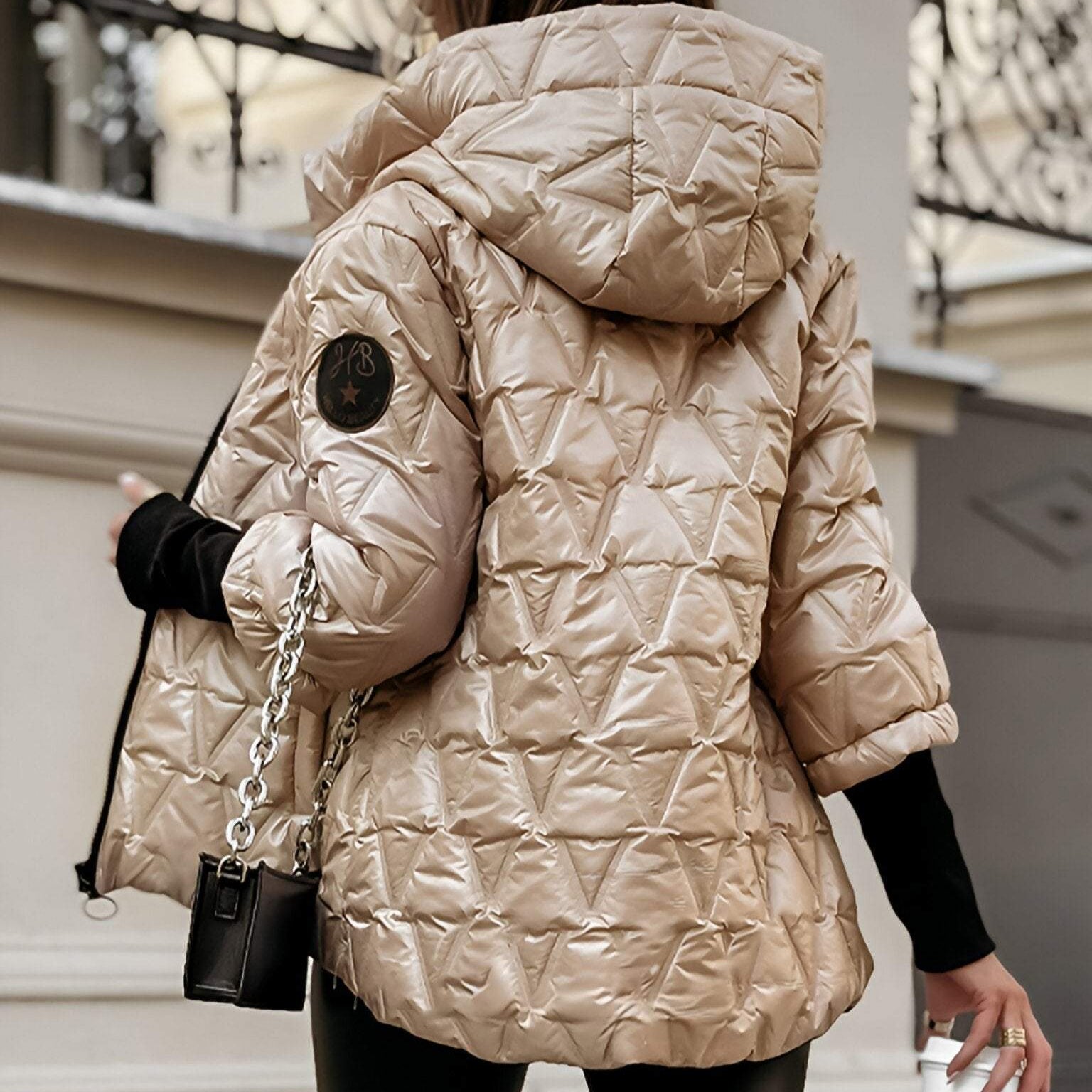 Giacca invernale trapuntata beige con cappuccio, design geometrico, maniche corte, indossata da una persona di spalle, moda autunno inverno.