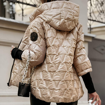 Giacca invernale trapuntata beige con cappuccio, design geometrico, maniche corte, indossata da una persona di spalle, moda autunno inverno.