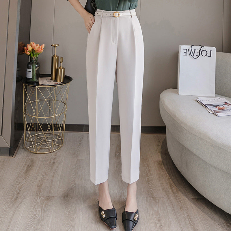 Pantaloni eleganti bianchi da donna, abbinati a mocassini neri con dettagli dorati. Arredamento moderno con tavolino dorato e divano grigio.