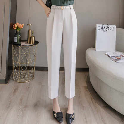 Pantaloni eleganti bianchi da donna, abbinati a mocassini neri con dettagli dorati. Arredamento moderno con tavolino dorato e divano grigio.