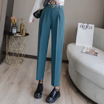 Pantaloni eleganti blu petrolio da donna, abbinati a scarpe nere chunky, in un salotto moderno con tavolino dorato e divano chiaro.