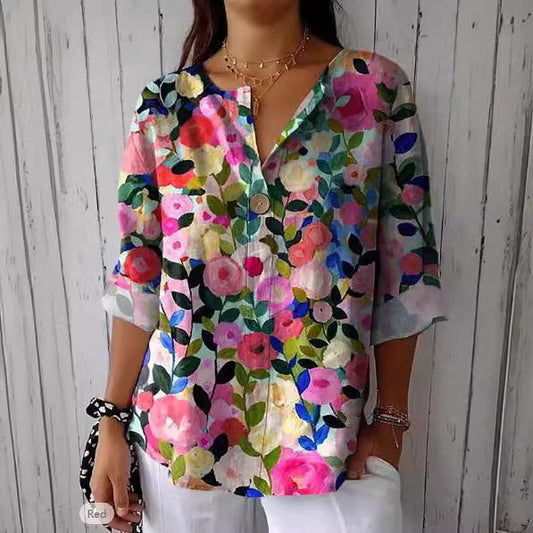 Blusa donna floreale colorata, maniche lunghe, sfondo legno bianco. Moda casual estiva, design vivace, abbigliamento femminile trendy.