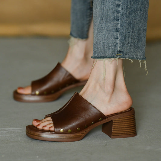 Sandali marroni in pelle con tacco largo, borchie decorative, indossati con jeans strappati. Scarpe moda donna, stile casual chic.