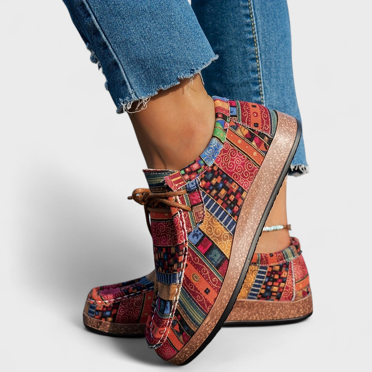 Scarpe colorate in tessuto patchwork con suola marrone, indossate con jeans strappati. Calzature moda donna, stile casual e vivace.