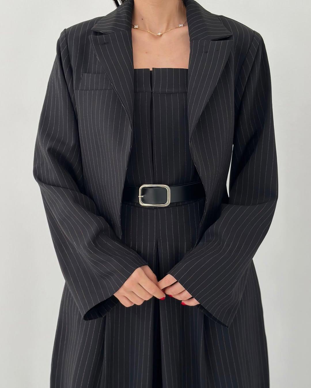 Donna in abito elegante nero a righe, con cintura in vita e giacca coordinata. Moda femminile, stile professionale, abbigliamento formale.