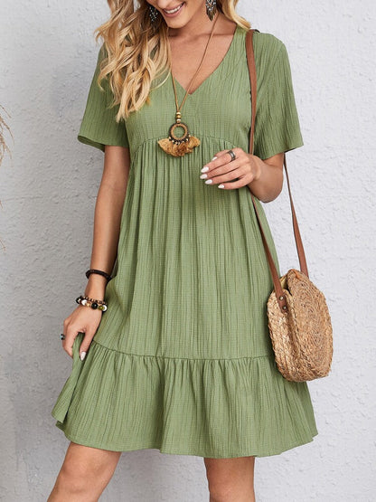 Donna con abito estivo verde, maniche corte, collana boho e borsa di paglia. Moda casual femminile, look estivo chic.