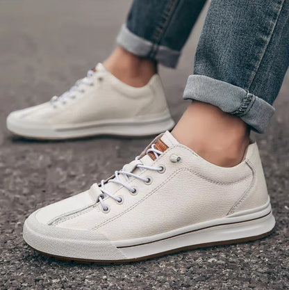 Scarpe da ginnastica bianche in pelle su strada asfaltata, indossate con jeans. Scarpe casual eleganti, moda urbana, comfort quotidiano.