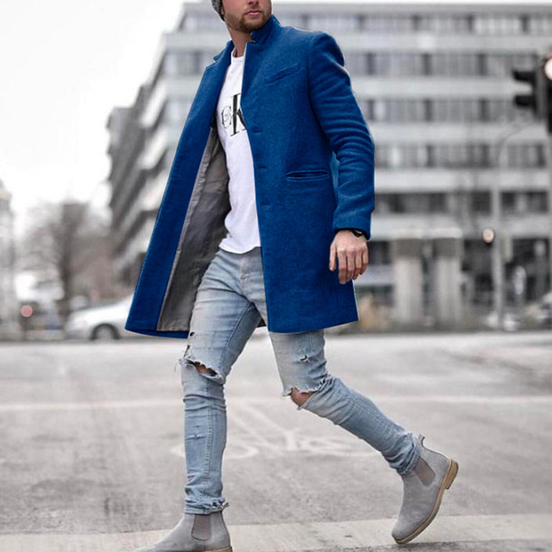 Uomo con cappotto blu elegante, jeans strappati e stivali grigi cammina in città. Moda maschile urbana, abbigliamento casual chic.