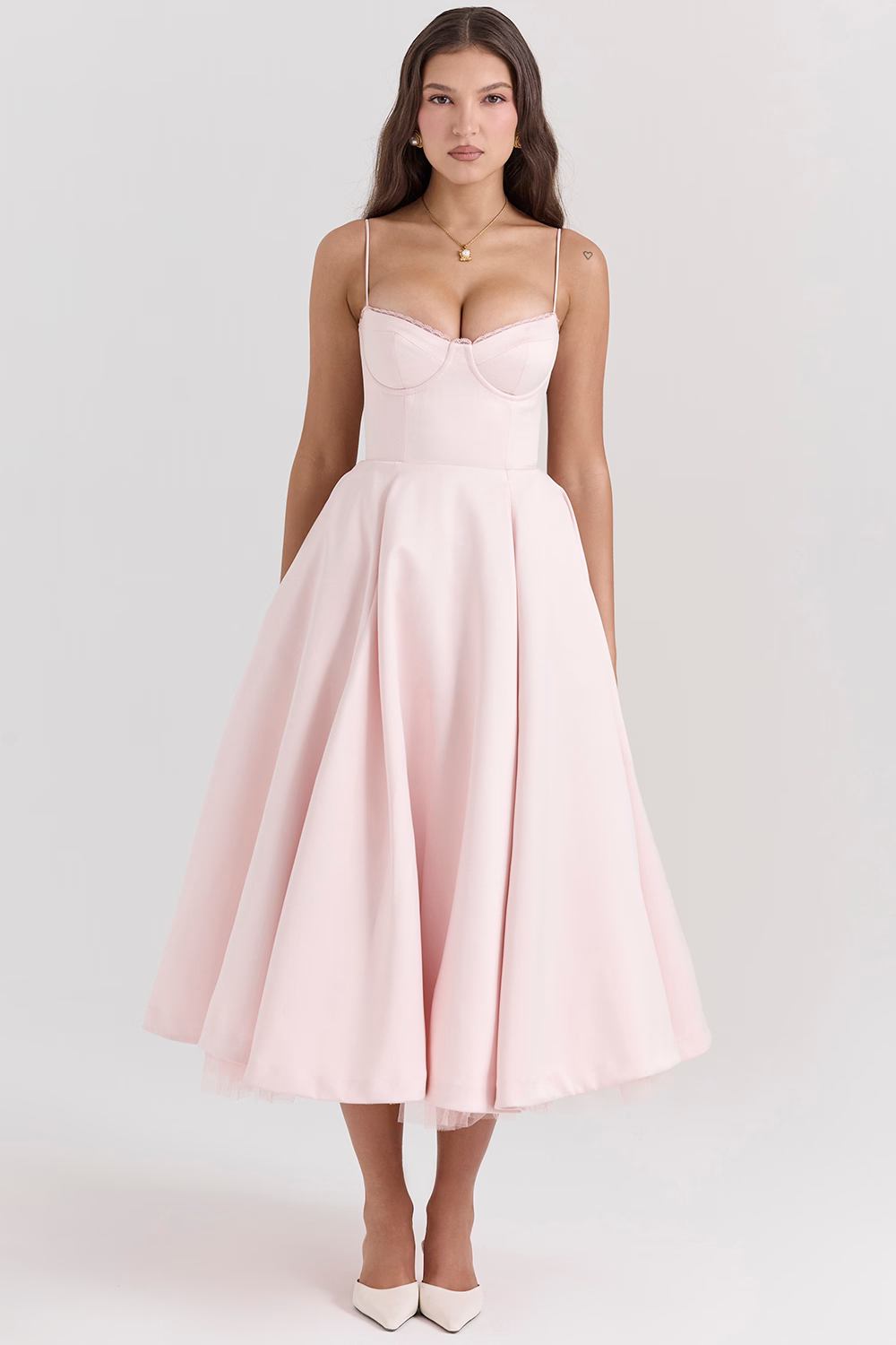 Donna in abito rosa chiaro elegante, lunghezza media, con spalline sottili e scollo a cuore, indossa scarpe bianche. Moda femminile, abbigliamento elegante.