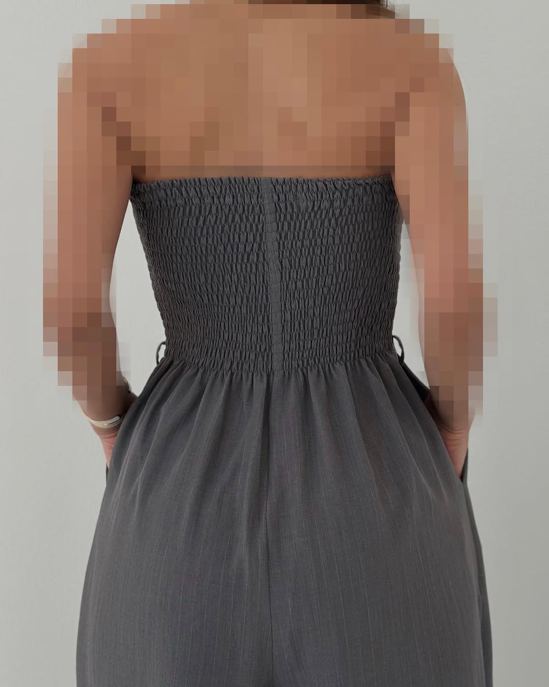 Donna in abito grigio senza spalline, tessuto arricciato, vista posteriore. Moda elegante, abbigliamento estivo, stile femminile moderno.