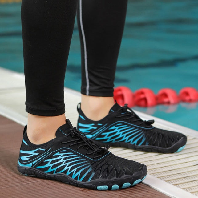 Scarpe da nuoto nere e blu con design a rete, indossate da una persona vicino a una piscina. Scarpe acquatiche leggere, ideali per sport acquatici.