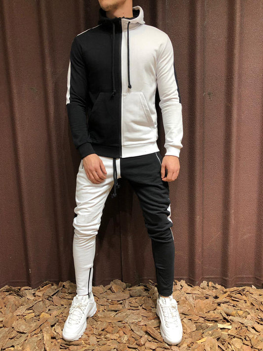 Tuta sportiva uomo bicolore bianco e nero, con cappuccio e pantaloni abbinati, indossata con scarpe da ginnastica bianche su sfondo marrone.