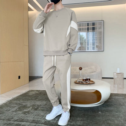 Uomo in tuta beige con strisce bianche, scarpe da ginnastica bianche, in salotto moderno. Arredamento minimalista, tavolino ovale, quadro astratto.