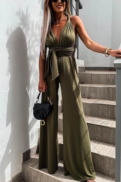 Donna con tuta verde oliva elegante, scollatura a V, cintura in vita, borsa nera, su scala moderna. Moda estiva, abbigliamento chic, stile urbano.