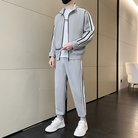 Uomo in tuta sportiva grigia con strisce nere, scarpe da ginnastica bianche, in piedi in un corridoio moderno. Moda casual, abbigliamento sportivo.