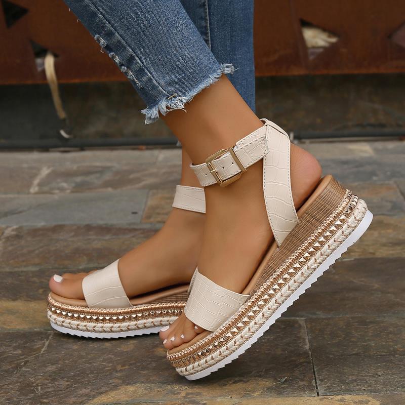 Sandali con zeppa beige, cinturino alla caviglia, dettagli intrecciati, suola bianca dentellata, indossati con jeans strappati.