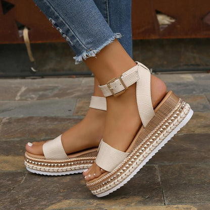 Sandali con zeppa beige, cinturino alla caviglia, dettagli intrecciati, suola bianca dentellata, indossati con jeans strappati.