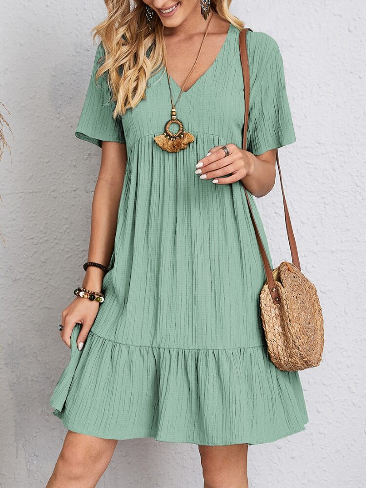 Donna con abito estivo verde, borsa a tracolla in paglia, collana boho e bracciali. Moda casual femminile, look estivo elegante.