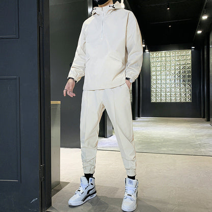 Uomo in tuta sportiva beige con cappuccio e scarpe da ginnastica bianche, in un corridoio moderno. Moda casual, abbigliamento sportivo elegante.