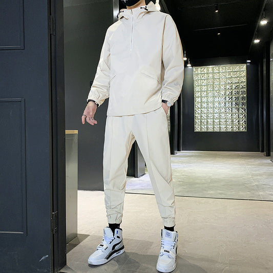 Uomo in tuta sportiva beige con cappuccio e scarpe da ginnastica bianche, in un corridoio moderno. Moda casual, abbigliamento sportivo elegante.