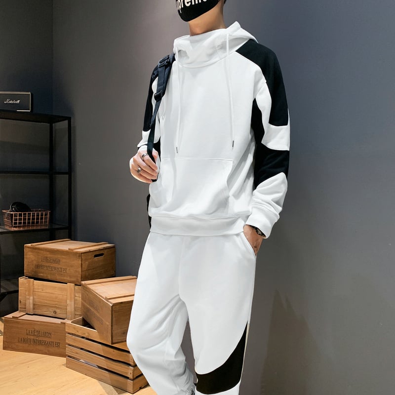 Uomo in tuta sportiva bianca e nera, con cappuccio, in piedi accanto a scatole di legno. Abbigliamento casual moderno, moda streetwear.