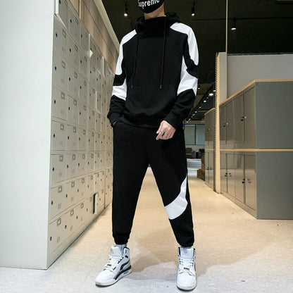 Uomo in tuta sportiva nera e bianca con cappuccio, scarpe da ginnastica bianche, in un ufficio moderno con armadietti metallici.