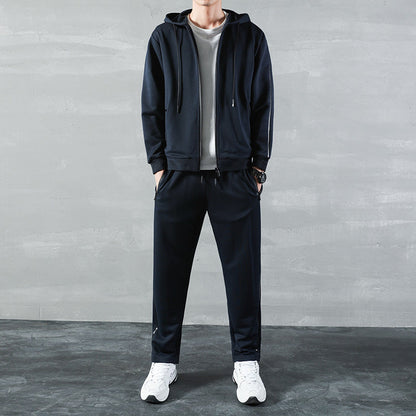 Uomo in tuta sportiva nera con felpa con cappuccio, t-shirt bianca e scarpe da ginnastica bianche, su sfondo grigio. Moda casual maschile.