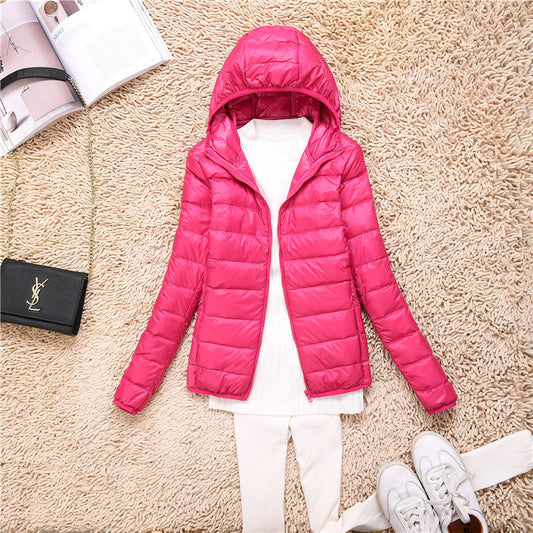 Giacca invernale rosa con cappuccio su tappeto beige, abbinata a maglia bianca e pantaloni chiari. Accessori: borsa nera e scarpe bianche.