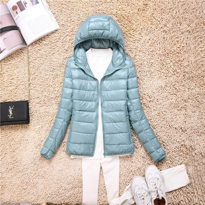 Giacca invernale imbottita azzurra con cappuccio su tappeto beige, abbinata a pantaloni bianchi e scarpe da ginnastica, moda casual donna.