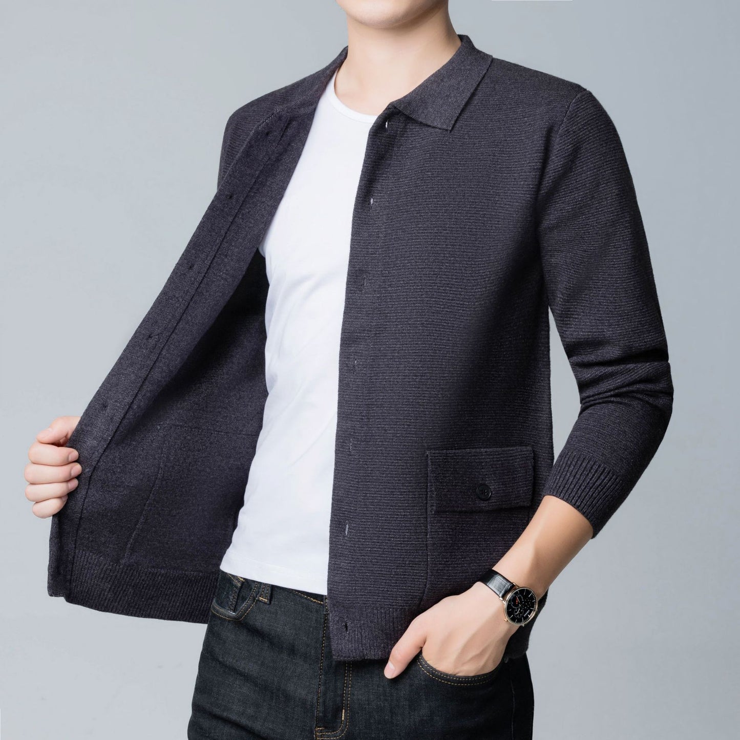 Uomo in camicia bianca e cardigan grigio scuro, orologio elegante al polso, moda casual maschile, abbigliamento autunnale, sfondo grigio chiaro.